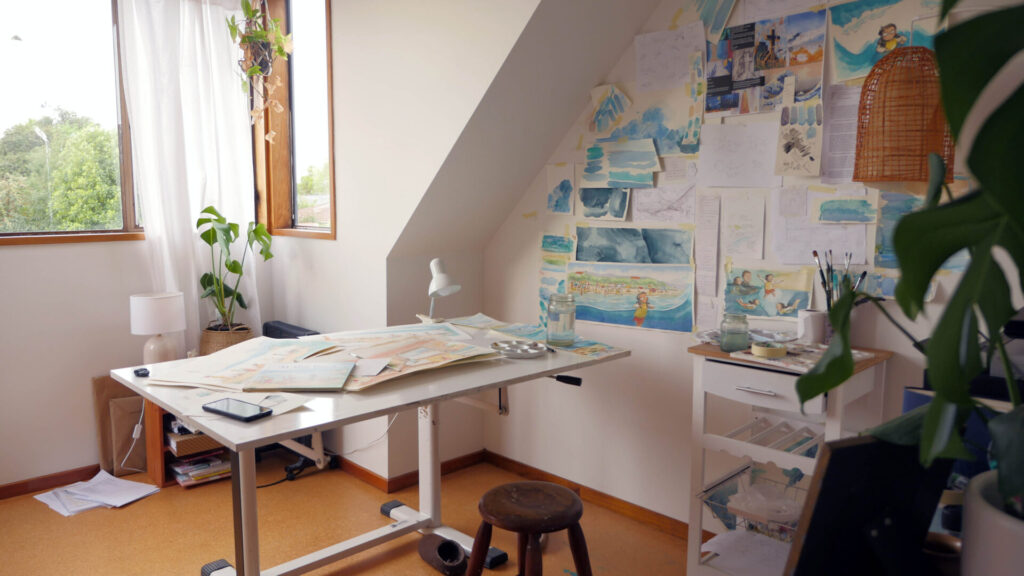 Photo of an art studio with a desk in the middle and art on the walls.